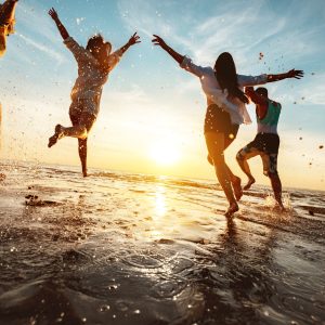 Four happy friends at sunset beach party runs to water