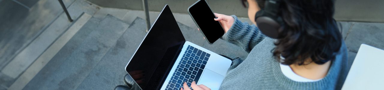 Close up portrait of girl, student works on laptop and listens music in headphones. Blank computer screen and hands typing on keyboard.